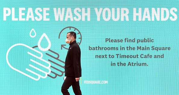 A man wearing a face mask walks past a sign urging people to wash their hands in Melbourne.