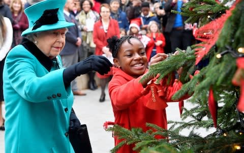 The Queen and Shylah Gordon-Clarke, aged eight, attach a bauble to a Christmas tree during her visit to Coram - Credit: Toby Melville/PA