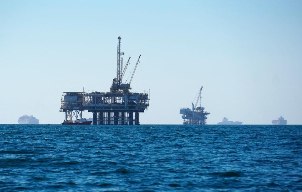 Cargo vessels are seen anchored offshore, sharing space with oil platforms, before heading into the Los Angeles-Long Beach port on Oct. 5, 2021. The Oregon State Treasury has at least $5.3 billion invested in fossil fuel companies, environmental groups said in a report on April 20, 2022, that blamed the state for adding to global warming and urged divestment.