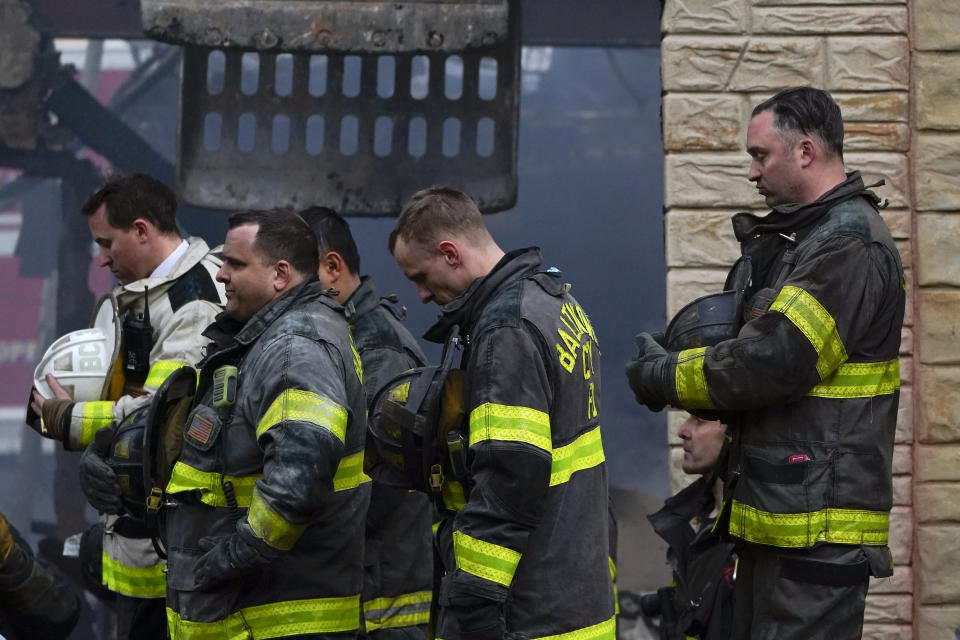 Firefighters bow their heads as a prayer is said after one of their own who died while battling a two-alarm fire in a vacant row home was pulled from the collapsed building, Monday, Jan. 24, 2022, in Baltimore. Officials said several firefighters died during the blaze. (AP Photo/Julio Cortez)