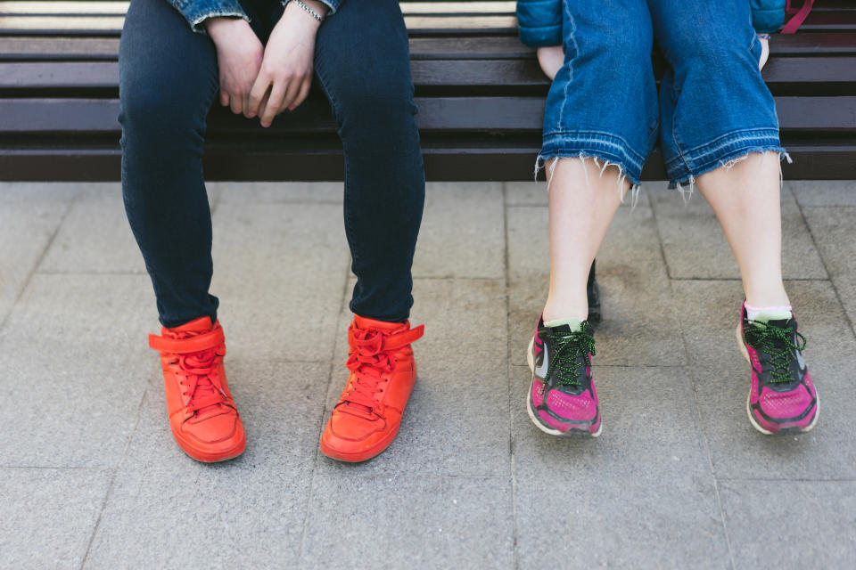 male and female legs in bright sneakers are sitting on a bench