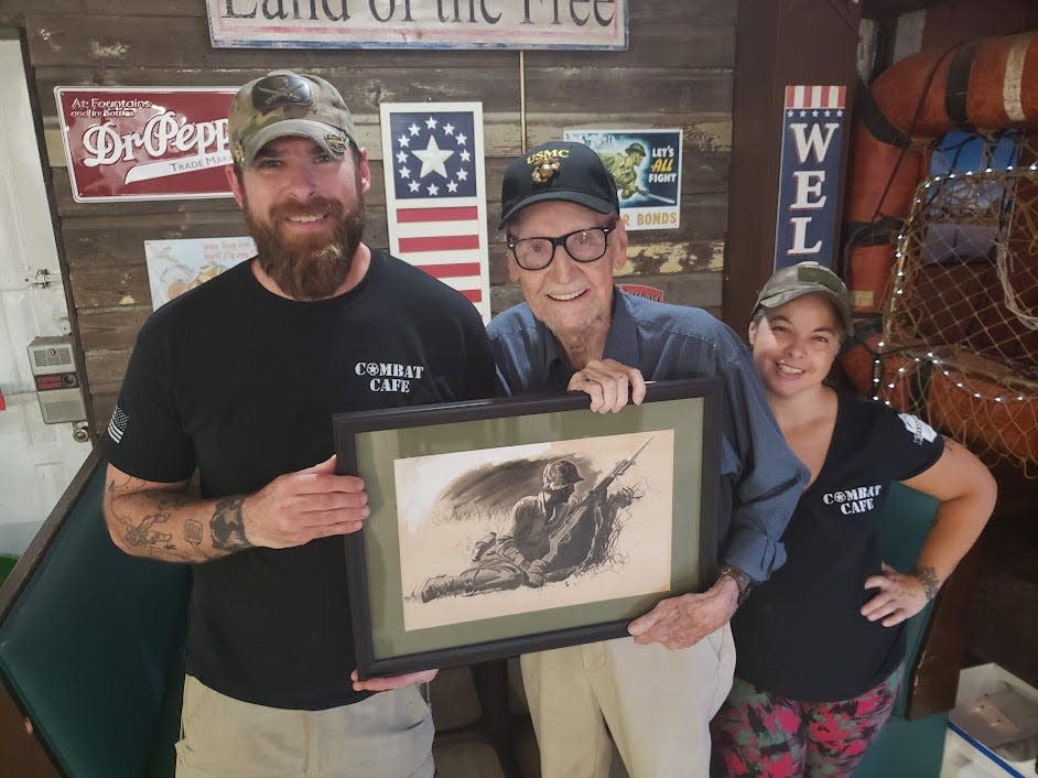 Former Marine Tech. Sgt. Gene Packwood presents an original Donald Dickson piece to Bruce and Beth Chambers for their military-themed setting at the Combat Cafe' on State Road 19 near Umatilla's south city limits.