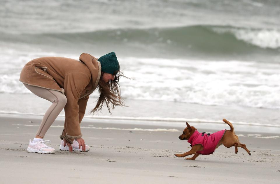 A woman plays with her dog on Long Beach, New York, on March 16. One loophole to shelter-in-place orders: You can still walk your dog.