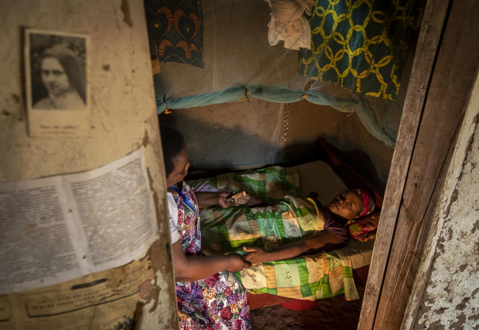 In this photo taken Tuesday, Nov. 5, 2019, palliative care nurse Madeleine Mukantagara, 56, left, prays with Vestine Uwizeyimana, 22, right, who has spinal degenerative disease and is taking oral liquid morphine for her pain, as she visits to check on her health at her home in the village of Bushekeli, near Kibogora, in western Rwanda. While people in rich countries are dying from overuse of prescription painkillers, people in Rwanda and other poor countries are suffering from a lack of them, but Rwanda has come up with a solution to its pain crisis - it's morphine, which costs just pennies to produce and is delivered to households across the country by public health workers. (AP Photo/Ben Curtis)