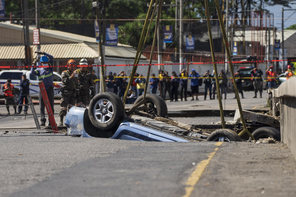 A vehicle is pulled from a sinkhole in Villa Nueva, Guatemala, Sunday, Sept. 25, 2022. Rescuers are searching for people who are believed to have fallen into the sinkhole while driving their vehicle, while four others were rescued alive from the scene on Saturday night. (AP Photo/Moises Castillo)