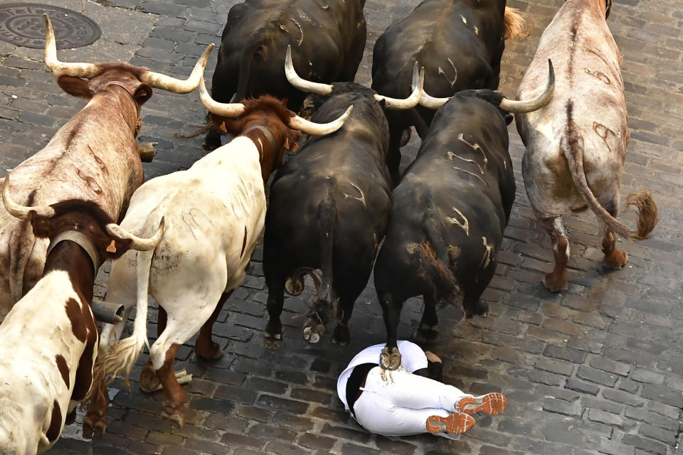 A runner falls as people run through the street with fighting bulls at the San Fermin Festival in Pamplona, northern Spain, Friday, July 8, 2022. Revellers from around the world flock to the city every year for nine days of uninterrupted partying in Pamplona's famed running of the bulls festival which was suspended for the past two years because of the coronavirus pandemic. (AP Photo/Alvaro Barrientos)