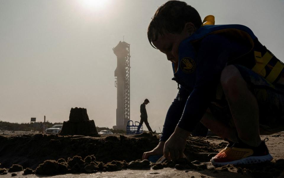 A boy builds a sandcastle on the beach as SpaceX's next-generation Starship spacecraft atop its powerful Super Heavy rocket