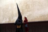 A penitent walks past a woman on his way to a church before taking part in the procession of "La Borriquita" brotherhood on Palm Sunday in the Andalusian capital of Seville, southern Spain, April 13, 2014. Holy Week is celebrated in many Christian traditions during the week before Easter. REUTERS/Marcelo del Pozo (SPAIN - Tags: RELIGION SOCIETY TPX IMAGES OF THE DAY)