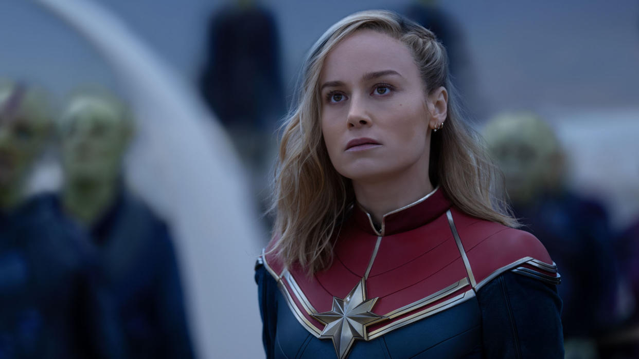  Carol Danvers look at something off-screen with some Skrulls behind her in The Marvels. 