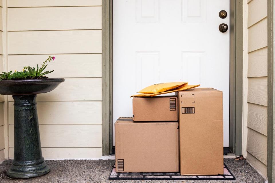 A pile of packages sit in front of a white front door. 