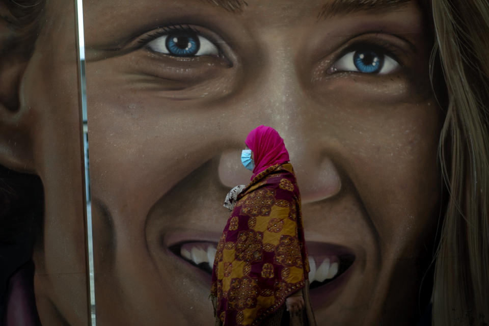 A woman wearing a mask to prevent the spread of the coronavirus walks past a graffiti in Barcelona, Spain, Monday, Oct. 19, 2020. Several Spanish regions adopt new restrictions to deal with the health emergency. Spain is nearing one million infections since the onset of the pandemic, the most in Europe. (AP Photo/Emilio Morenatti)