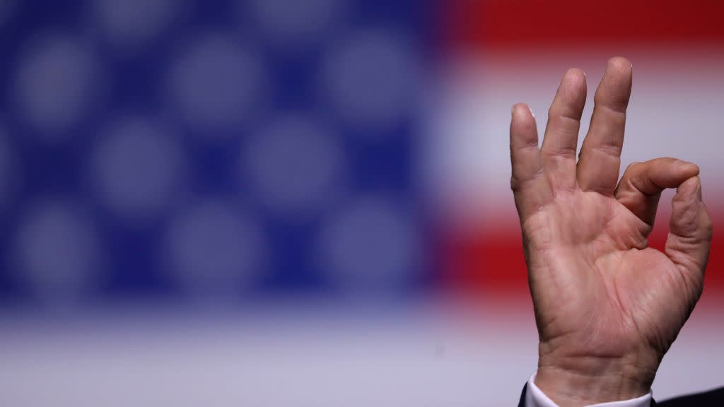 Trump's hand making "ok" gesture with US flag in background (no faces).