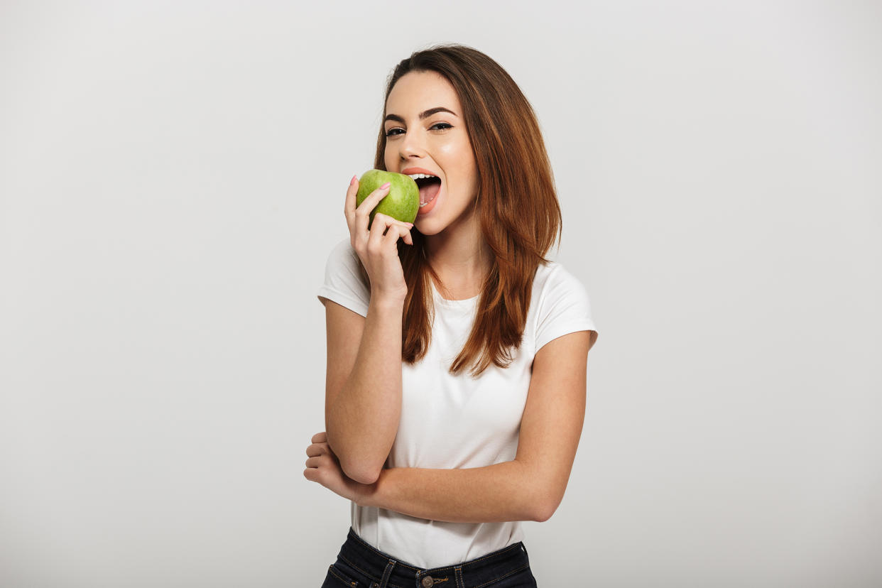 Chrysti Ane joyfully eating a green apple against a white background