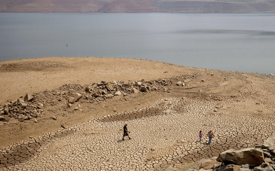 FILE — In this Aug. 22, 2021, file photo, a family walks over cracked mud near Lake Oroville's shore as water levels remain low due to continuing drought conditions in Oroville, Calif. State water officials are preparing to tell major urban and agricultural water agencies on Friday, March 18, 2022, that they'll get even less water from state supplies than the small amount they were promised at the start of the year. Lake Oroville is currently 68% of its historical average supply.(AP Photo/Ethan Swope, File)