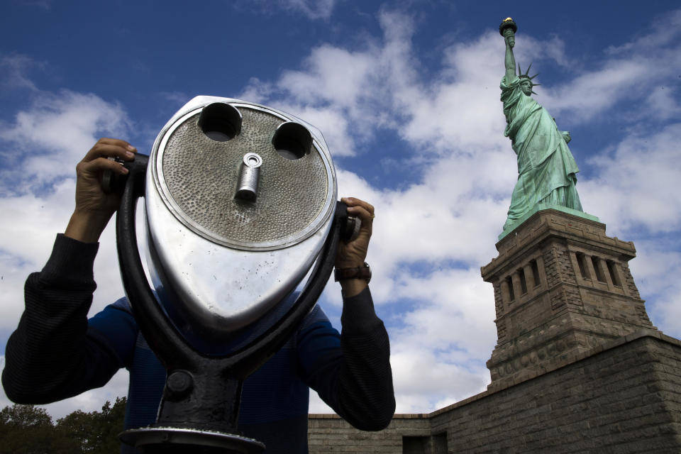 FILE - In this Oct. 13, 2013, file photo, the Statue of Liberty looms over a visitor as he uses binoculars to look out onto New York Harbor in New York. (AP Photo/John Minchillo, File)