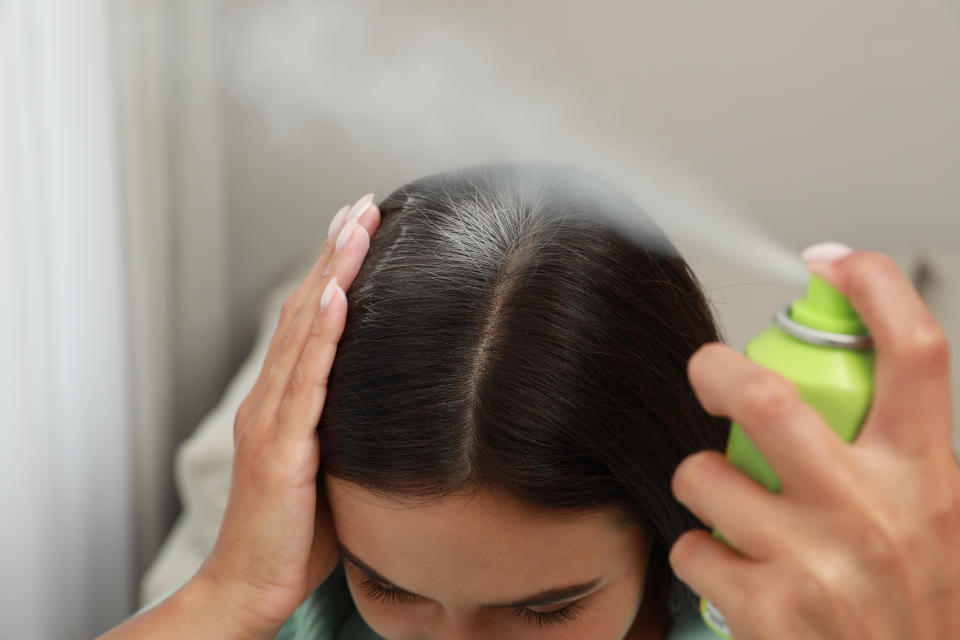 Woman applying dry shampoo onto her hair, closeup