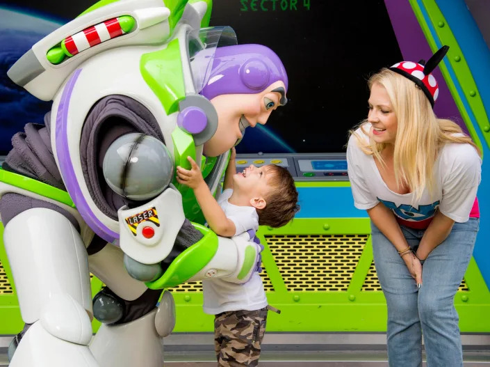 A worker in a Buzz Lightyear costume hugging a little boy while Melissa smiles at them.