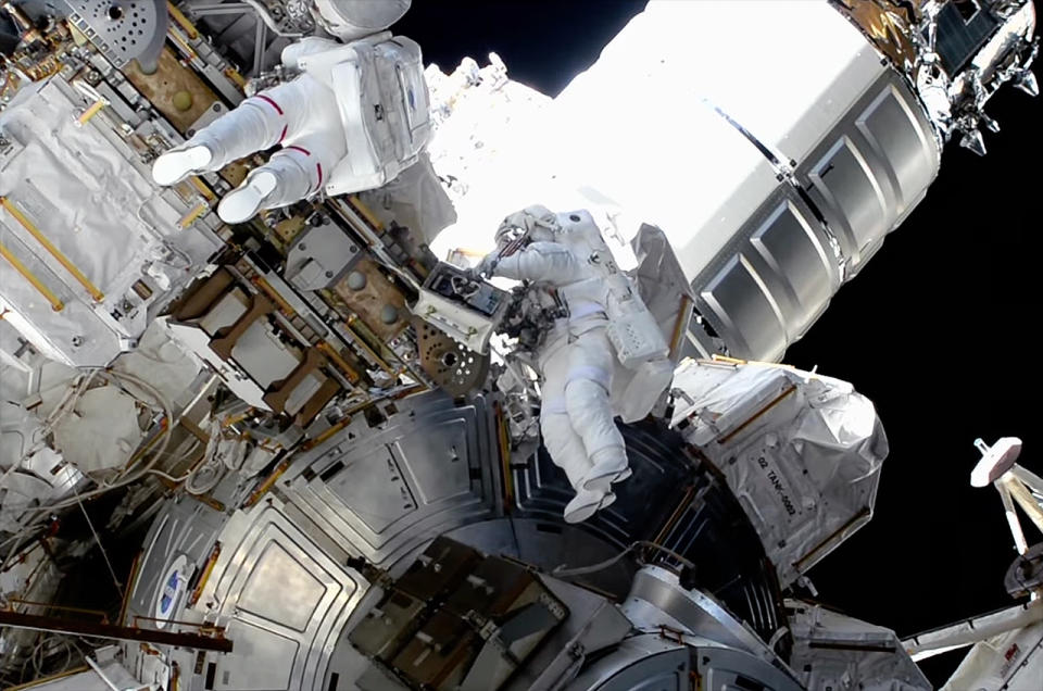 two astronauts in spacesuits on the outside of a space station with Earth in the background