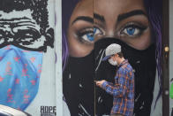 A pedestrian wearing a mask to protect against the spread on COVID-19 passes murals painted on a boarded-up business in downtown Austin, Texas, Tuesday, March 9, 2021. Texas Gov. Greg Abbot's mask mandate for the state ends Wednesday. (AP Photo/Eric Gay)