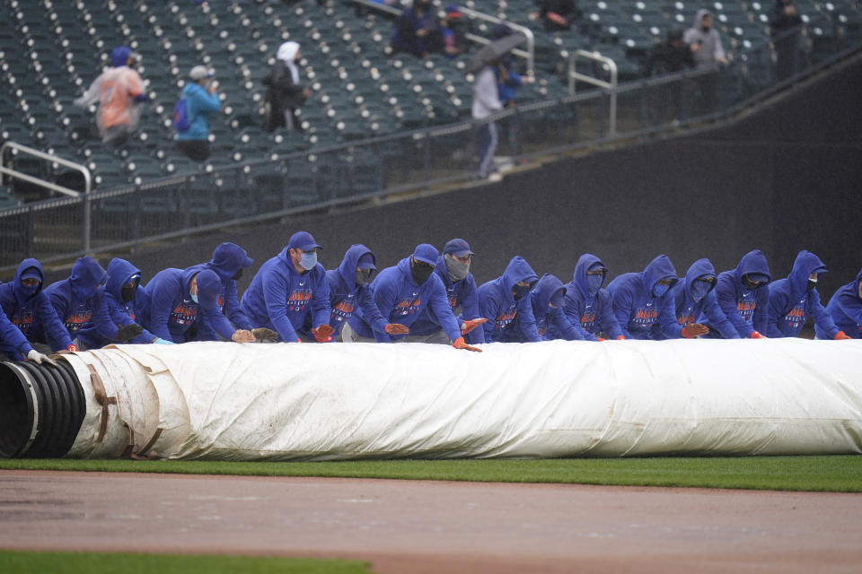 New York Mets employees roll a tarp over the field during a delay in the first inning of a baseball game against the Miami Marlins at Citi Field, Sunday, April 11, 2021, in New York. The game was delayed at the top of the first inning due to rain. (AP Photo/Seth Wenig)