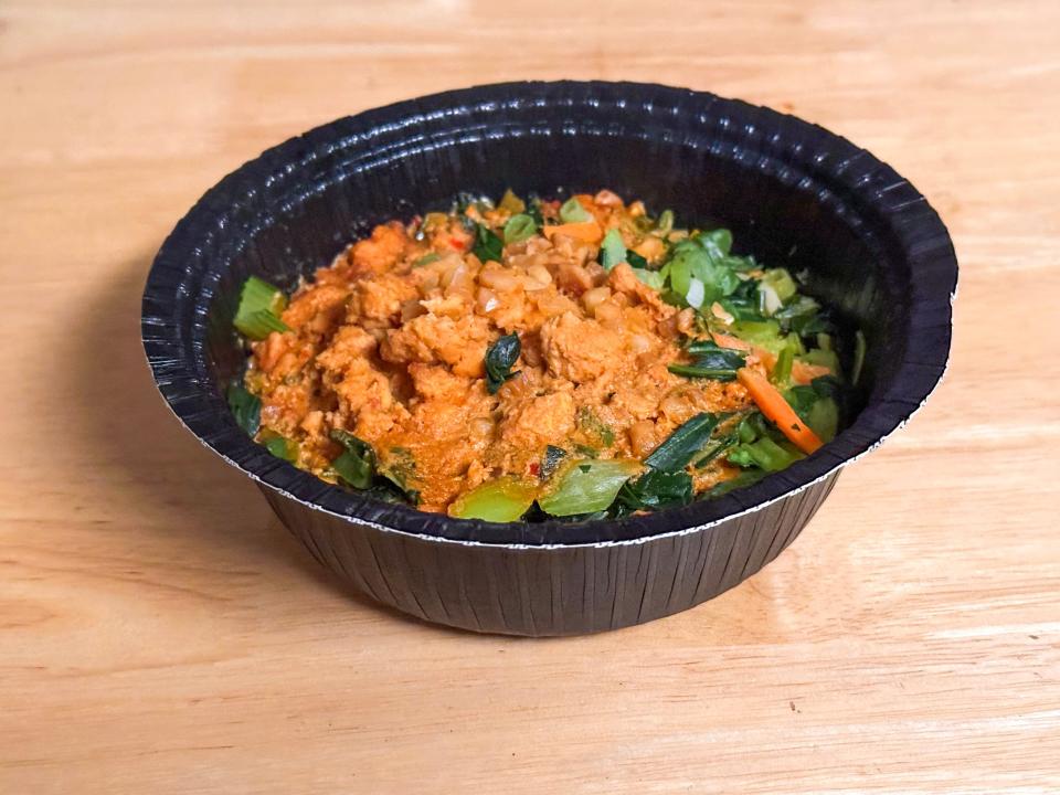 A black bowl filled with noodles, green vegetables, sliced carrots, and a red-orange sauce