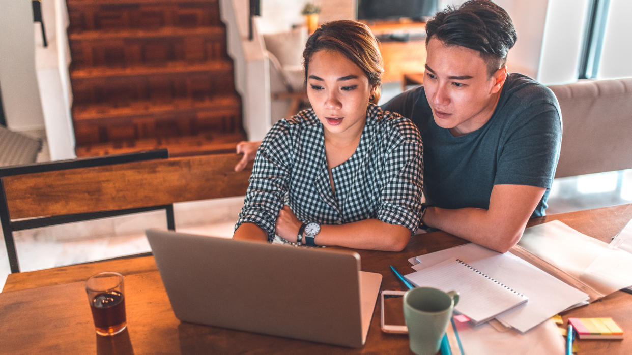 Serious young couple planning budget over laptop at table.