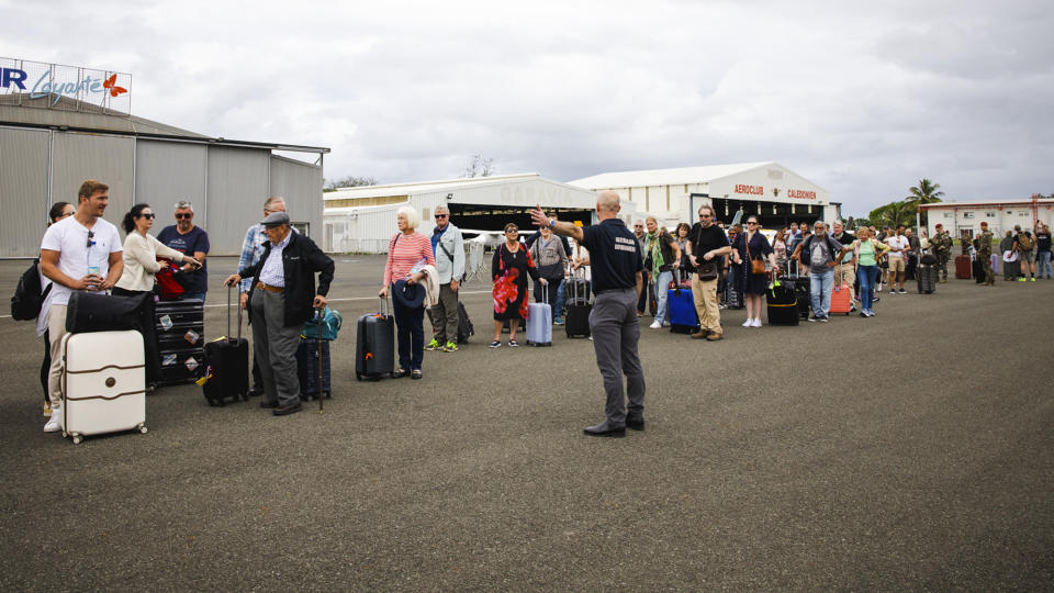 In this photo provided by the Australian Department of Defence, an official from the Department of Foreign Affairs and Trade (DFAT) gestures to Australian and other tourists as they prepare to depart from Magenta Airport in Noumea, New Caledonia, Tuesday, May 21, 2024. Australia and New Zealand have sent airplanes to New Caledonia to begin bringing home stranded citizens from the violence-wracked French South Pacific territory. (LAC Adam Abela/Royal Australian Airfare via AP)
