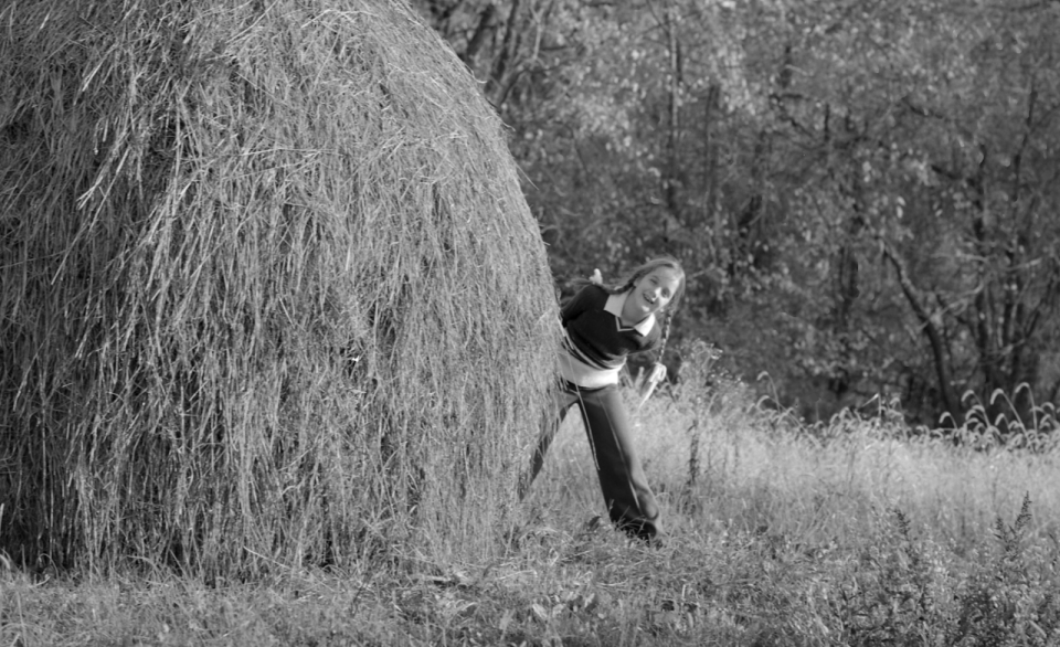 The author, captured by her mother, next to a haystack at their family home her stepfather named “Omega Farm.”