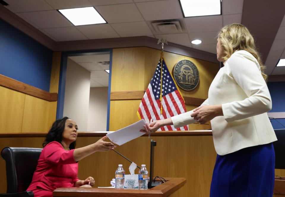 Attorney Ashleigh Merchant hands documents to attorney Fani Willis who testifies in a hearing in the case of State of Georgia v. Donald John Trump at the Fulton County Courthouse in Atlanta, Georgia, U.S., February 15, 2024.