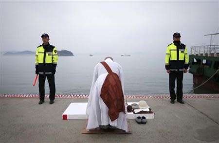 Two policemen stand guard as a priest says prayers at the port in Jindo, where family members are waiting for bodies recovered from the capsized passenger ship Sewol April 22, 2014. REUTERS/Kim Hong-Ji