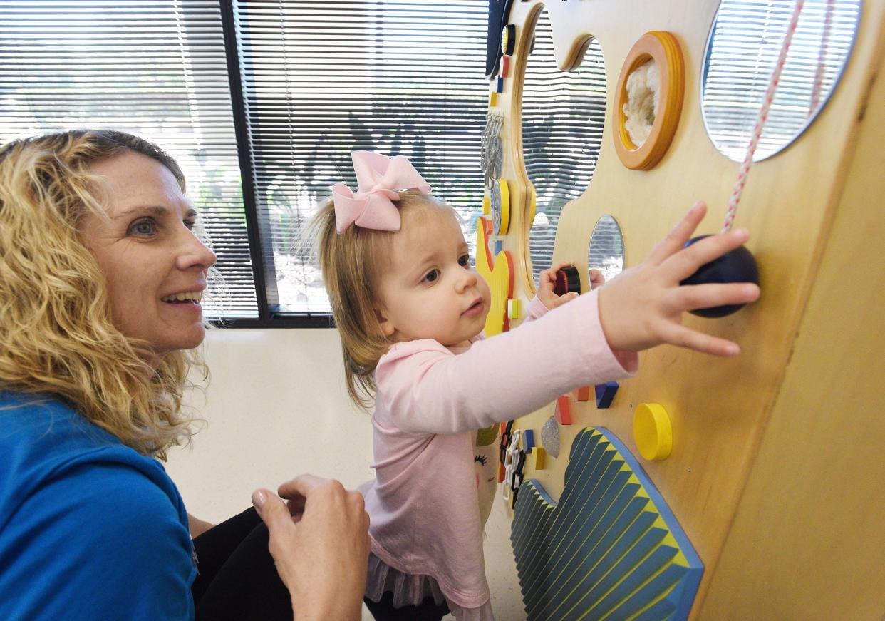 An occupational therapist, left, works with a toddler as she explores the sensory wall in the Therapy Gym during a session at Wolfson Children's Rehabilitation Autism and Neurodevelopment Center.