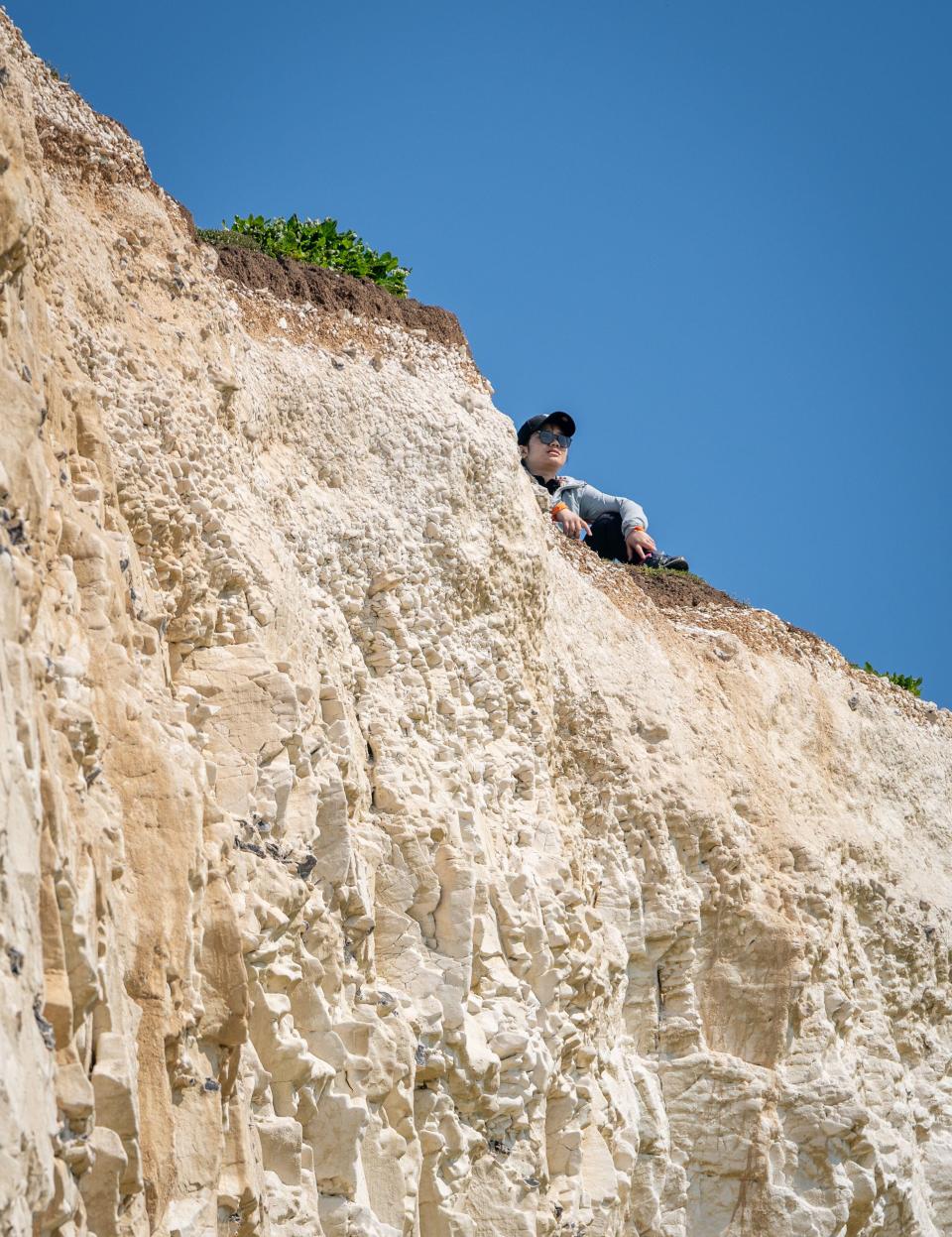 Beachy Head, East Sussex, UK. 11 May, 2024. A tourist sits on the crumbling cliff edge 3oo feet up on the coast near Birling Gap as temperature are predicted to hit 27C today on hottest weekend of the year so far. Beachy Head, East Sussex, UK Credit: reppans/Alamy Live News