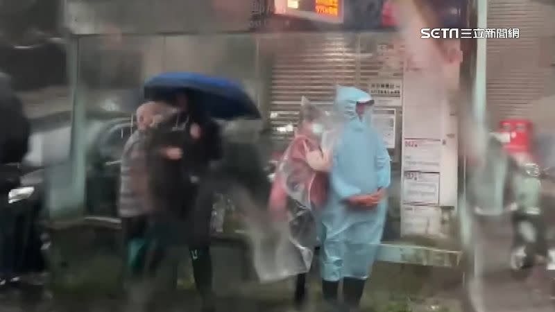 在公車亭等車光撐傘根本擋不住大雨，因此有民眾穿上了雨衣。