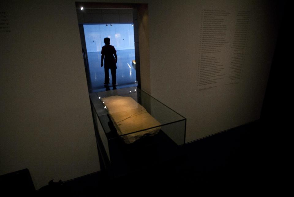 A museum worker walks next to the 'Gabriel Stone' as it is displayed at an exhibition at the Israel Museum in Jerusalem, Tuesday, April 30, 2013. An ancient stone with mysterious Hebrew writing and featuring the archangel Gabriel is being displayed in Israel, even as scholars continue to argue about what the inscription means. (AP Photo/Sebastian Scheiner)