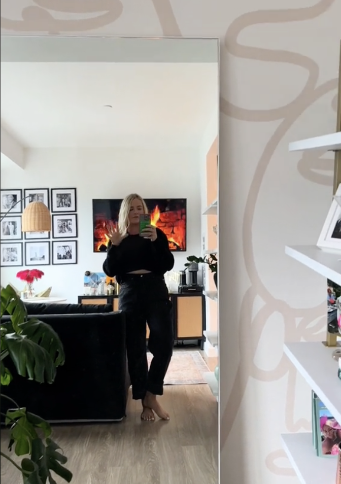 Woman taking a mirror selfie in a casual black outfit with a living room background