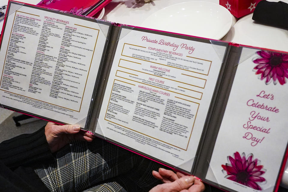 Jamie Cygielman, general manager and president of American Girl, opens a menu at the store's cafe, Friday, Dec. 2, 2022, in New York. Starting early this year, Mattel's American Girl Cafe added more adult fare like beet and goat cheese salads and cocktails like Aperol spritzes and Bloody Mary's after seeing adults show up without children. (AP Photo/Bebeto Matthews)