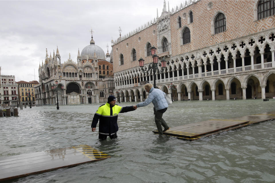 A city worker helps a woman who decided to cross St. Mark's Square on a gangway, in spite of it being closed, in Venice, Italy, on Nov. 17, 2019.&nbsp; (Photo: ASSOCIATED PRESS)