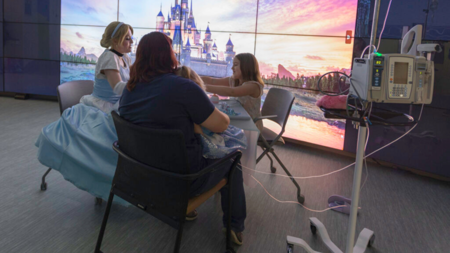 Cinderella hosts a tea party with a patient, Aria (seated on her mom’s lap), age 3, and her older sister, Caroline, in front of our beautiful monitor wall with a famous castle on display. (HSHS St. Vincent Children's Hospital)