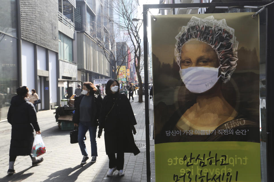 People wearing face masks to help protect against the spread of the coronavirus walk by an advertisement for a hair shop along a shopping street in Seoul, South Korea, Sunday, Jan. 31, 2021. (AP Photo/Ahn Young-joon)