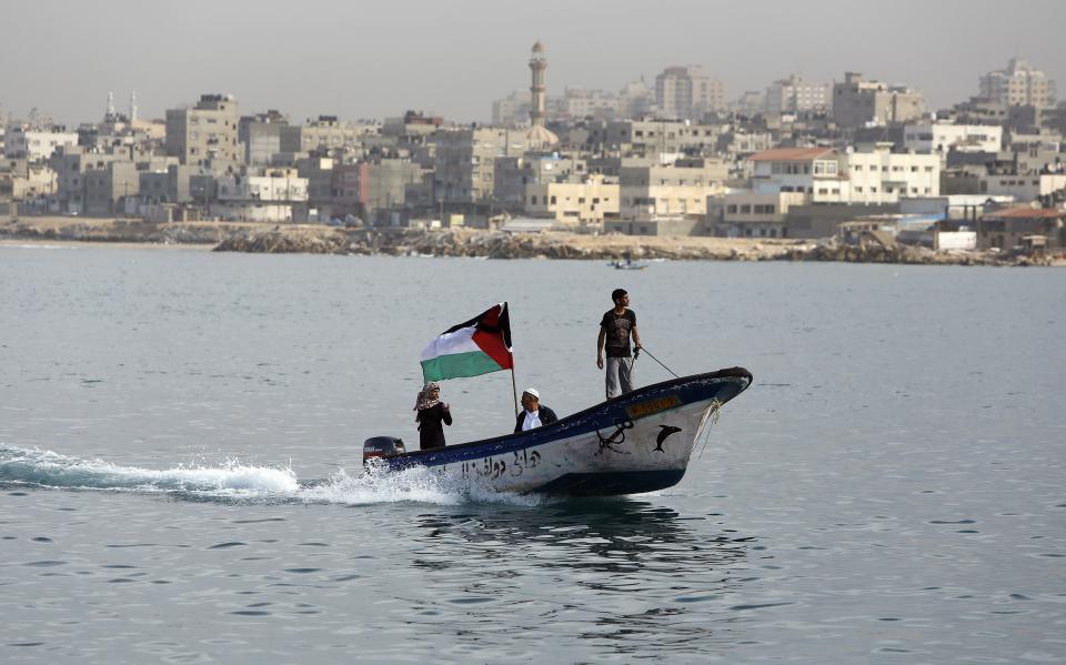 Palestinians ride a boat as a national flag flutters during a protest against the blockade on Gaza, at the seaport of Gaza City