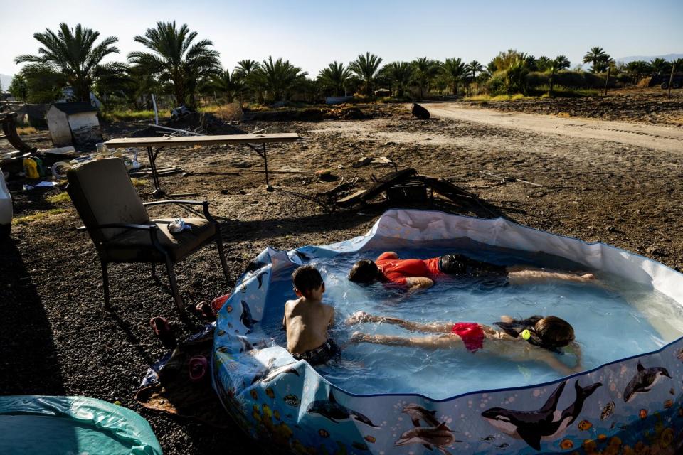 Three children, two swimming, in a portable wading pool