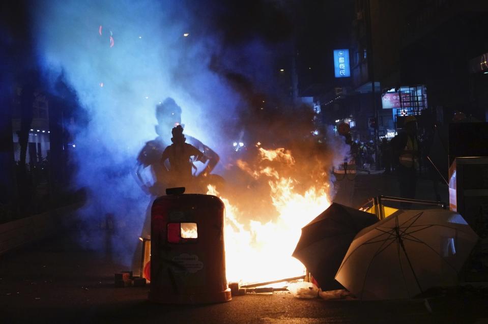 A journalist stands next to fire set by protesters in Hong Kong, Sunday, Sept. 29, 2019. Protesters and police clashed in Hong Kong for a second straight day on Sunday, throwing the city's business and shopping belt into chaos and sparking fears of more ugly scenes leading up to China's National Day this week.. (AP Photo/Vincent Yu)