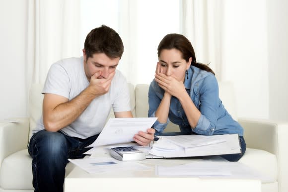 Couple looking at sheet of paper and covering mouths as if gasping