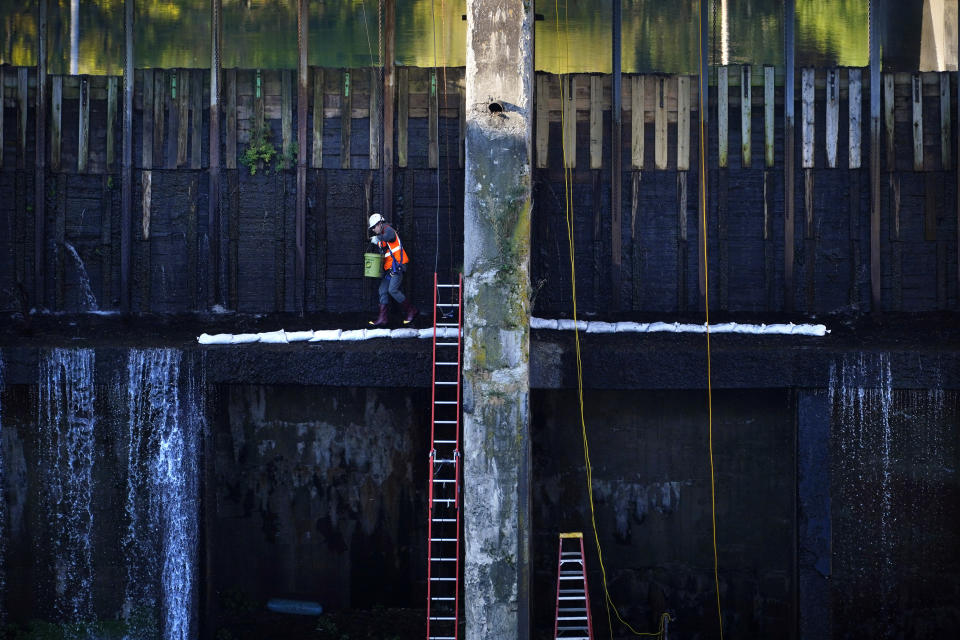 A worker places a line of sand bags on the downstream wall of a dam at Weston Station on the Kennebec River, Tuesday, Sept. 14, 2021, in Skowhegan, Maine. The dam has provided hydro-electric power for over 100 years. (AP Photo/Robert F. Bukaty)