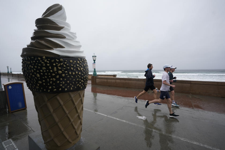 A group runs past Belmont Park as rain engulfs the area, Tuesday, March 21, 2023, in San Diego. Californians are tired. Tired of the rain, tired of the snow, tired of stormy weather and the cold, relentlessly gray skies that have clouded the Golden State nearly nonstop since late December. (AP Photo/Gregory Bull)