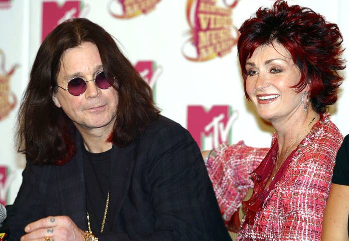 Two individuals at an event posing for the camera; the person on the left wears sunglasses and a dark shirt, the one on the right has short, spiky hair