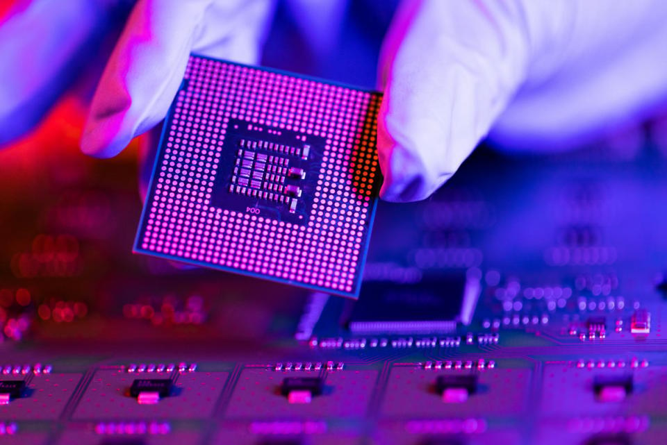 White gloves handling a computer chip above a circuit board.