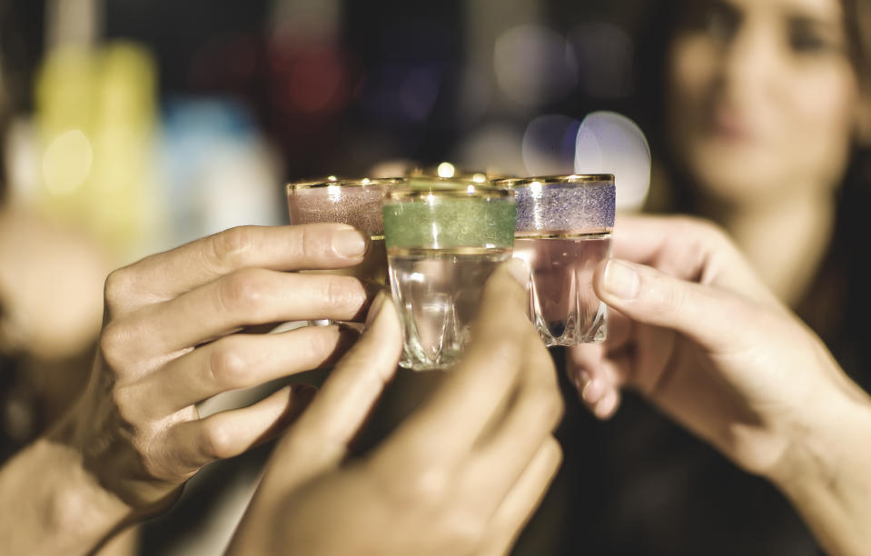 a close up of four people toasting with shot glasses