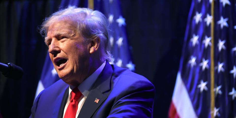 Donald Trump standing at a podium in front of two American flags.