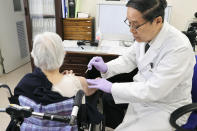 An elderly woman receives her first dose of Pfizer's COVID-19 vaccine at a special nursing home in Nagasaki, southwestern, Japan, Monday, April 12, 2021. Japan started its vaccination drive with medical workers and expanded Monday to older residents, with the first shots being given in about 120 selected places around the country. (Kyodo News via AP)